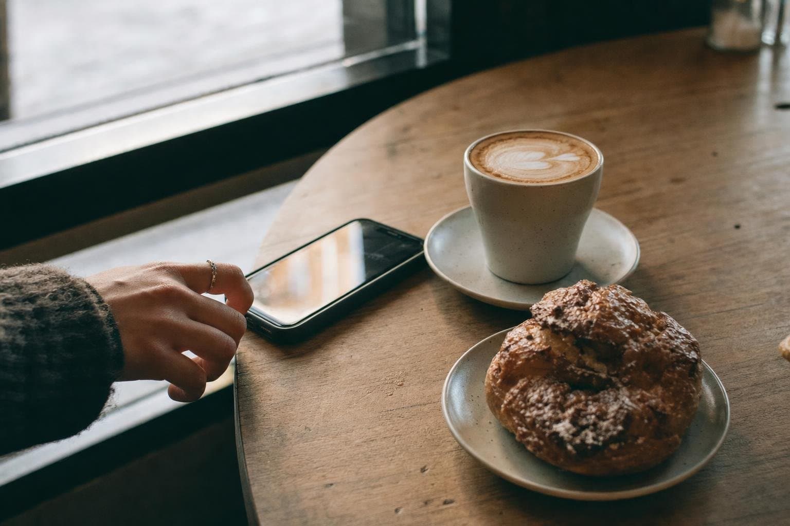 A phone lighting up on a cafe table next to a coffee and pastry
