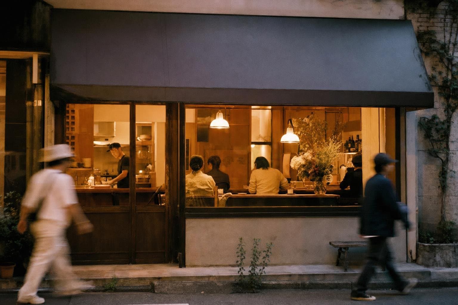 A warm restaurant storefront glowing at dusk seen from the sidewalk
