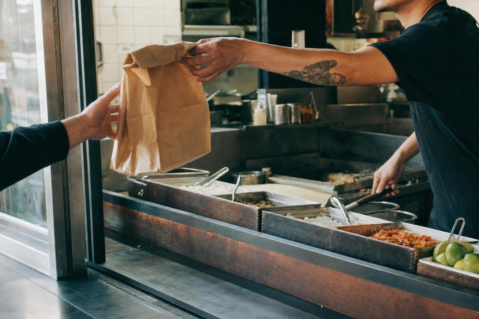 A bag of food handed across a bright quick-service restaurant counter