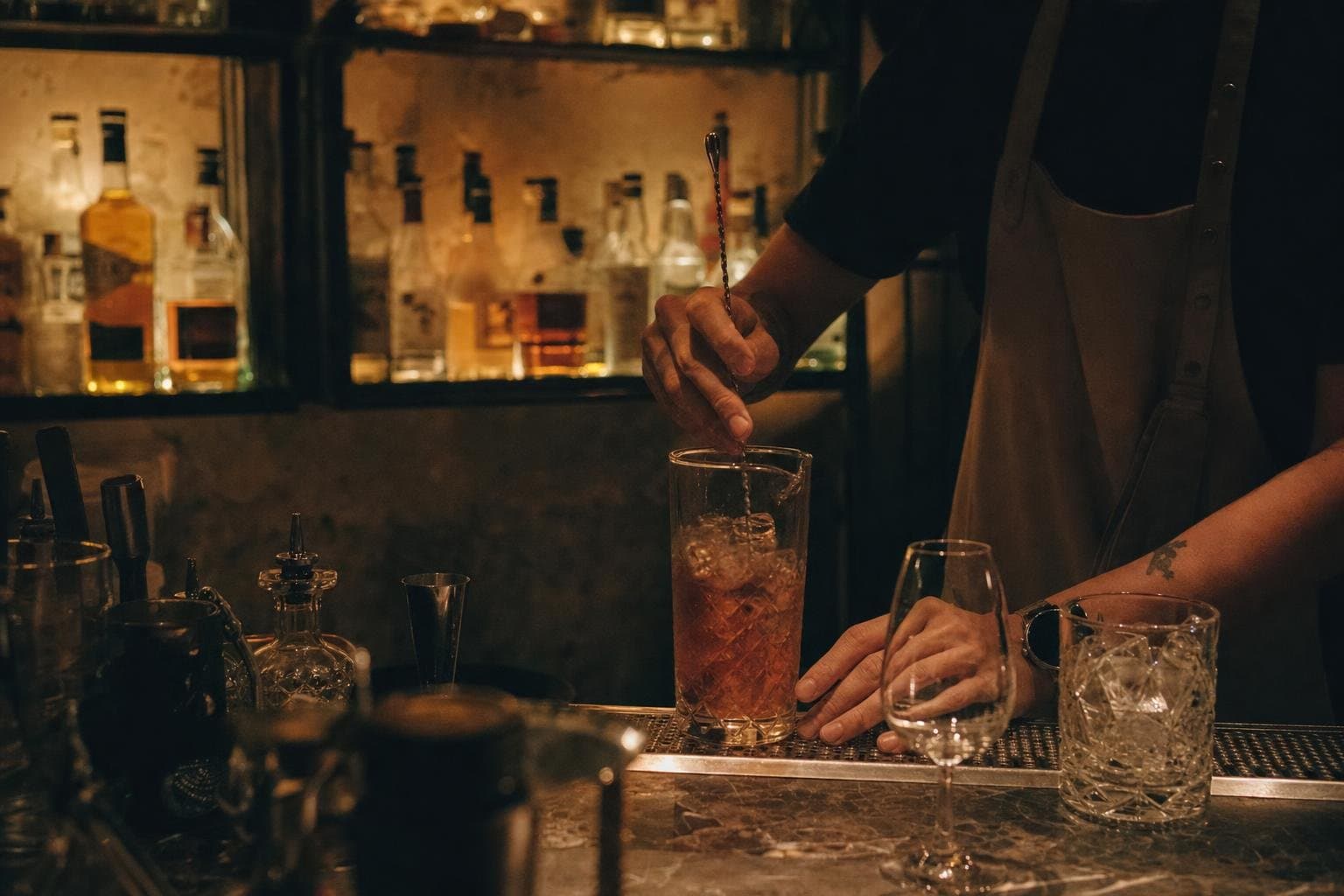 A bartender stirring a cocktail in a moody, backlit evening bar