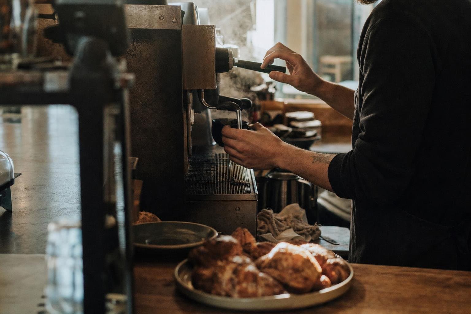 A barista pulling an espresso shot in the morning light of a small coffee shop