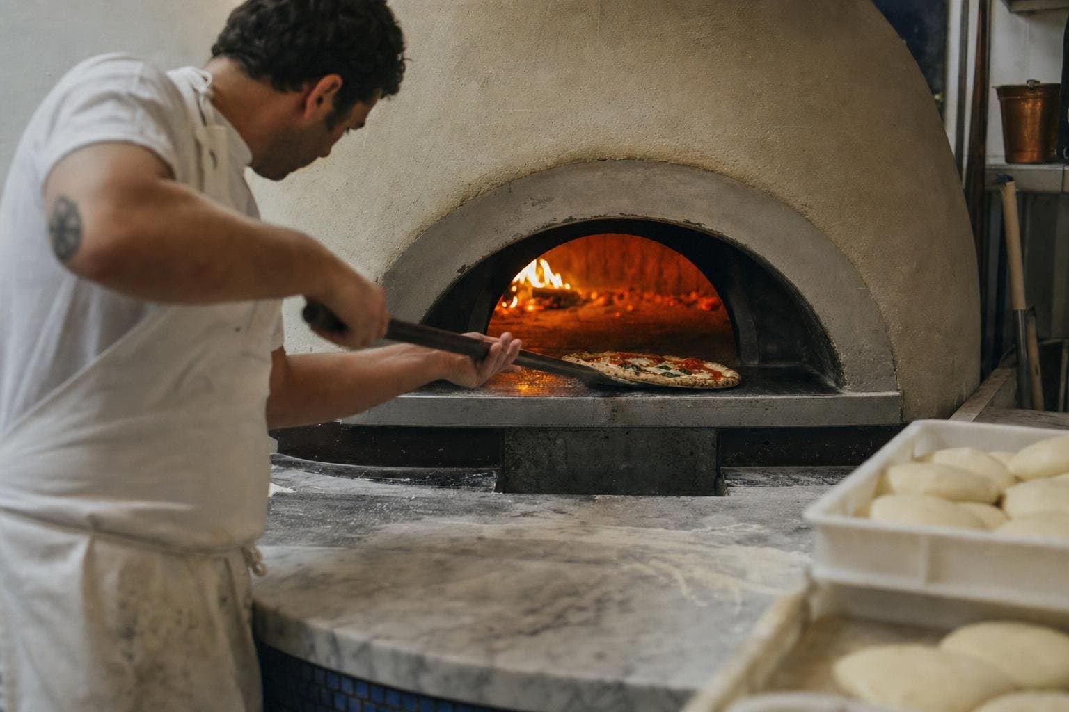 A pizzaiolo sliding a pizza into a glowing wood-fired oven at an independent pizzeria